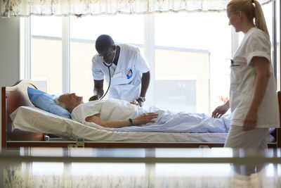 Nurse looking at male colleague examining senior man in hospital ward