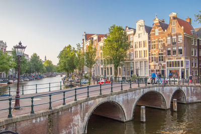 Bridge over river by buildings in city against clear sky