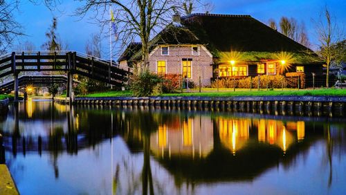 Illuminated building by lake against sky at night