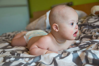 Cute baby boy looking away lying on bed at home