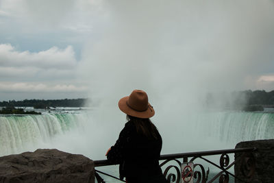 Rear view of woman looking at waterfall against sky