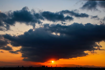 Low angle view of sunlight streaming through clouds during sunset