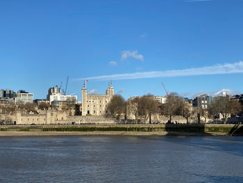 Buildings by river against blue sky