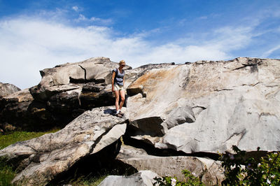 Low angle view of woman sitting on rock against sky