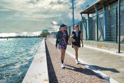 Two beautiful girls happily walk on a seaside promenade on a summer day