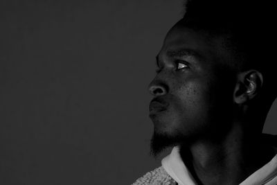 Portrait of young man looking away against black background