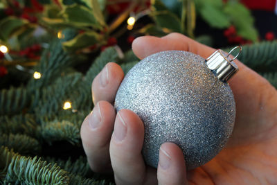 Close-up of hand holding bauble against christmas tree