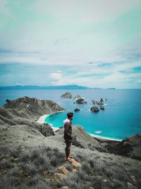 Man standing on rock by sea against sky