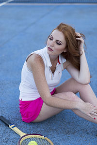 Woman with badminton racket sitting on playing field