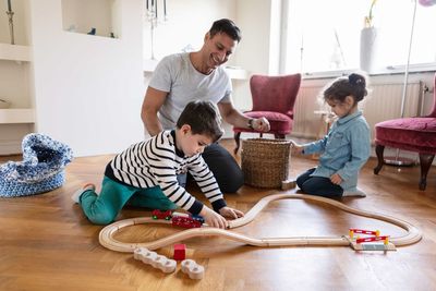 Son playing with miniature train while smiling father and sister kneeling on floor at home