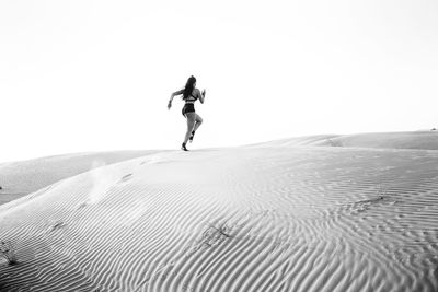 Full length of man jumping on sand dune against sky