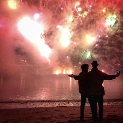 Silhouette man and woman standing on beach against sky at night