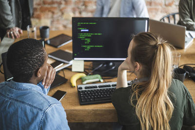 Rear view of male and female colleagues coding over computer at startup company