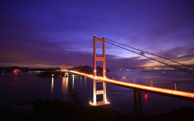 Illuminated bridge over river against sky at night