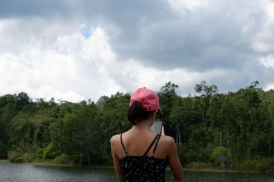 Rear view of woman standing by trees against sky