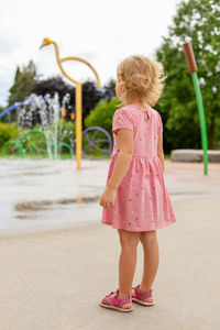 Little girl playing at splash pad playground in park in summer. child from behind near fountain