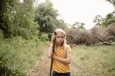 Portrait of cute girl holding stick while standing on land in forest