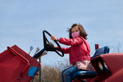 Girl in a mask pretending to drive a tractor at the county fair exhibit