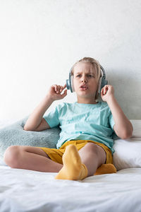 Cute boy listening to music in earphones seating on bed. child wearing headphones listens to music.