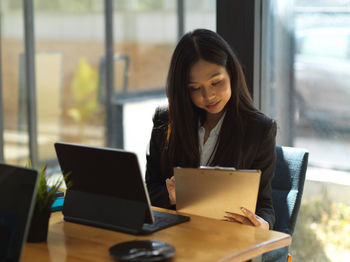 Young businesswoman holding clipboard while sitting at office
