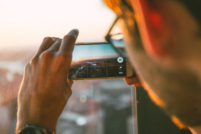 Close-up of man using mobile phone against sunset sky