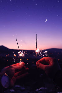 Close-up of person holding sparklers against sky during sunset