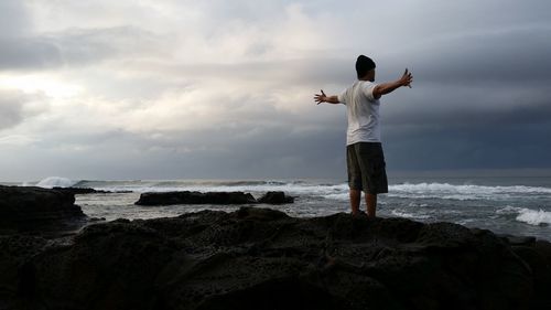 Man with arms outstretched standing on rock at beach
