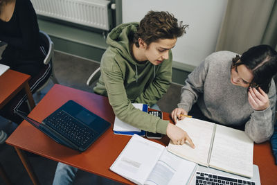 High angle view male student assisting female classmate at desk in classroom