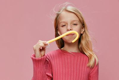 Portrait of young woman holding lollipop against pink background