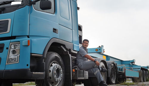 Portrait of man sitting on car against sky