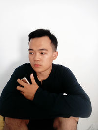 Portrait of young man sitting against wall