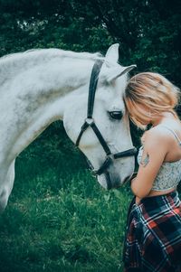 Side view of young woman standing by horse on field