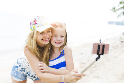 Cheerful mother and daughter taking selfie at beach