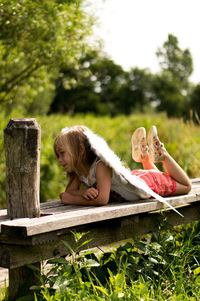 Girl wearing costume wings relaxing on wooden bench at park