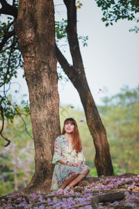 Portrait of young woman sitting on tree trunk