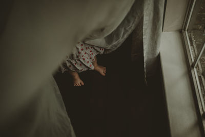 High angle view of playful girl hiding amidst curtains by window at home