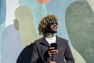 Smiling man holding mobile phone against wall