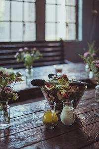 Refreshing salad and flower vase on wooden table by window