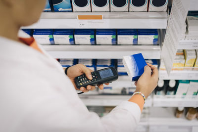 Midsection of male pharmacist using bar code reader on medicine standing by rack at store