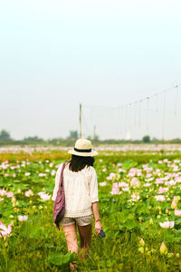 Rear view of woman walking on grassy field against sky