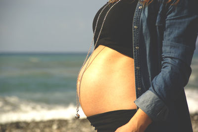 Midsection of pregnant woman standing at beach