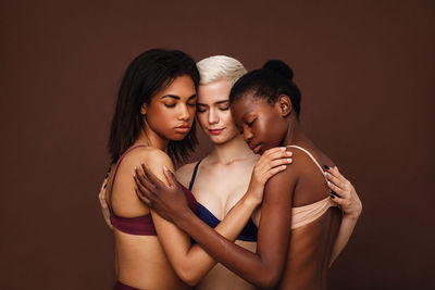 Multi-ethnic women embracing each other against brown background