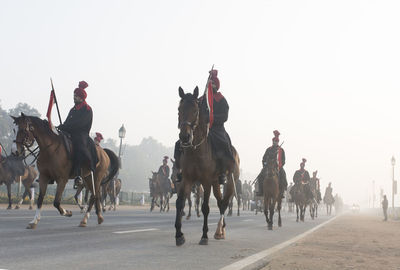 People riding horses on landscape against clear sky