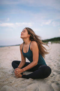 Young woman sitting on shore at beach against sky