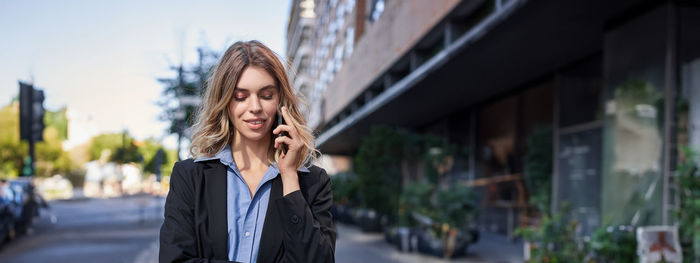 Portrait of young woman standing against building