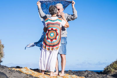 Senior couple standing with sarong at beach against sky