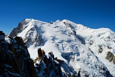 Scenic view of snowcapped mont blanc against clear blue sky, climbers and rescue helicopter.