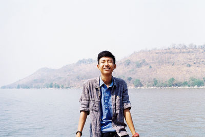 Portrait of young man standing on mountain against clear sky