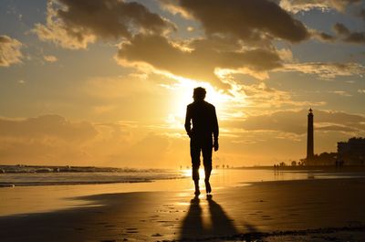 Silhouette of man walking on beach against sky during sunset