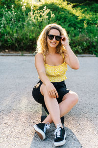 Young woman wearing sunglasses sitting on road